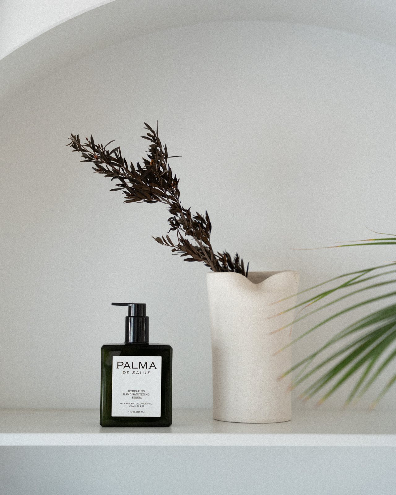 Hydrating Hand Sanitizing Serum on a white plaster shelf beside a ceramic vase