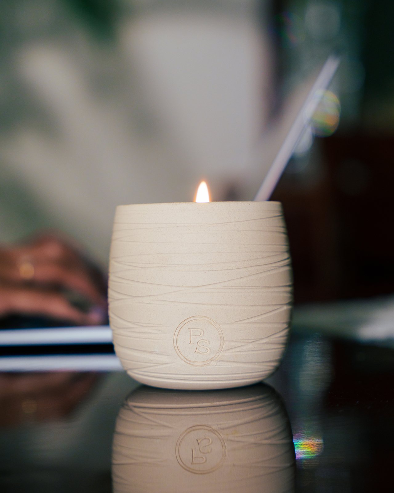 A lit candle on a desk beside a laptop