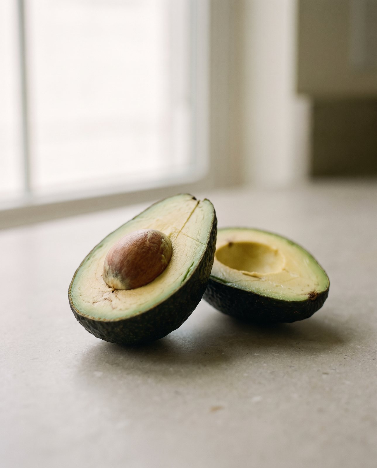 A halved avocado on stone in soft window light