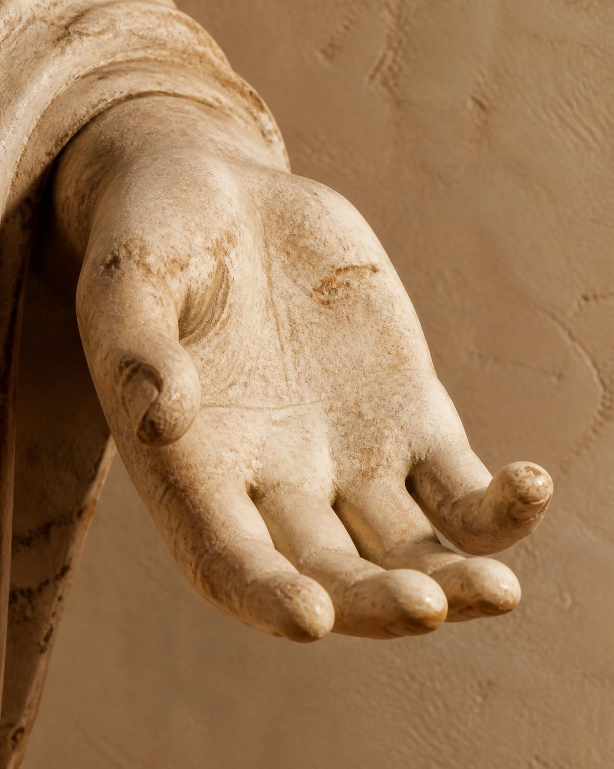 Close view of a weathered classical marble hand fragment, open palm catching warm sunlight